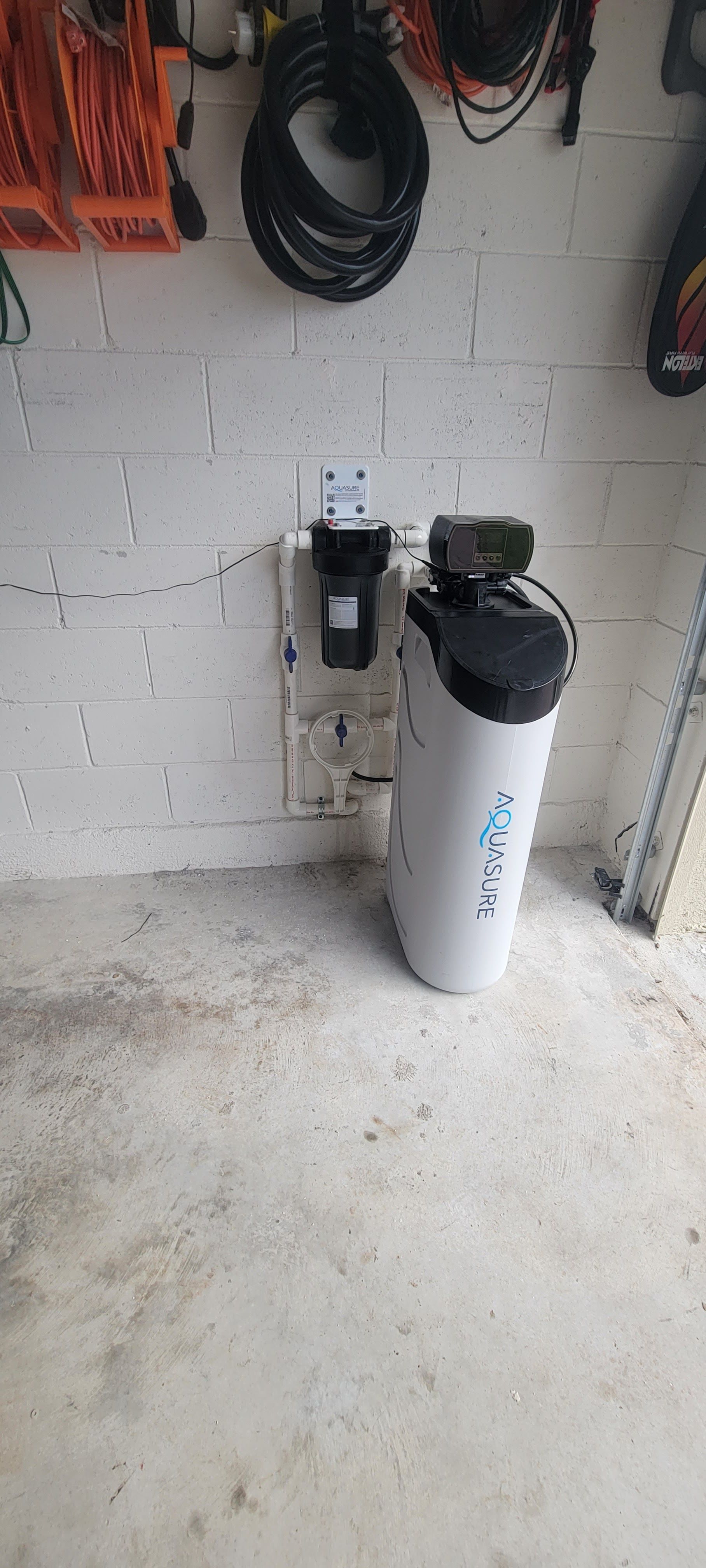 A water softener is sitting in a garage next to a brick wall.