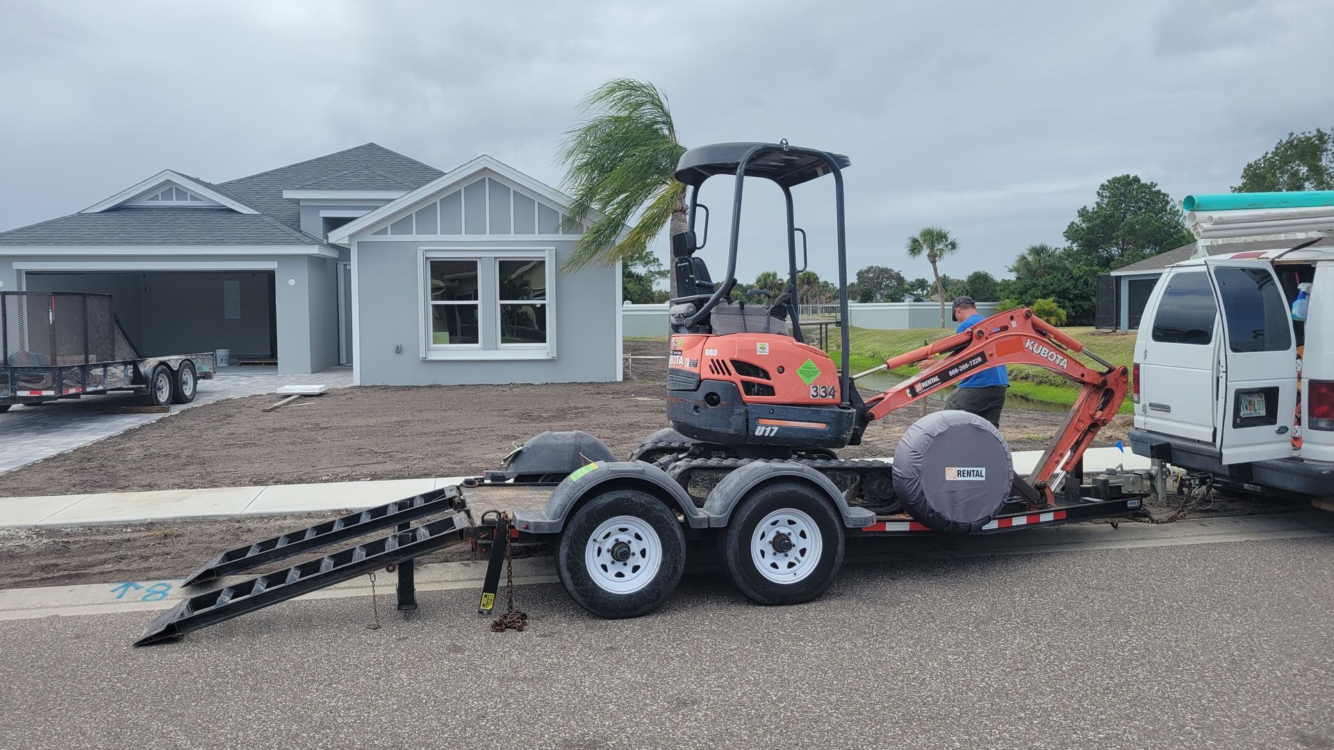 A trailer with a tractor on it is parked in front of a house.