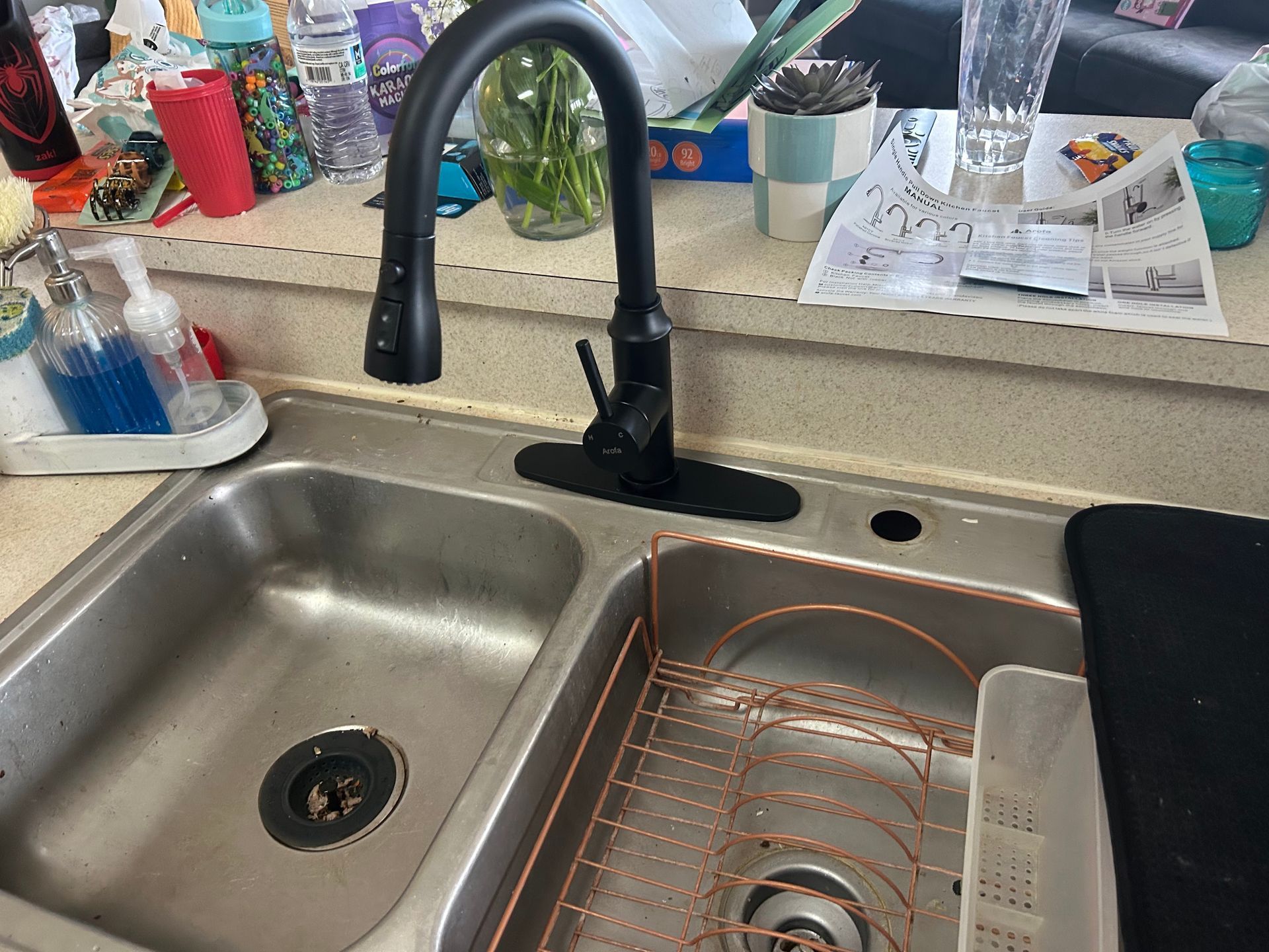 A kitchen sink with a black faucet and a copper dish rack.