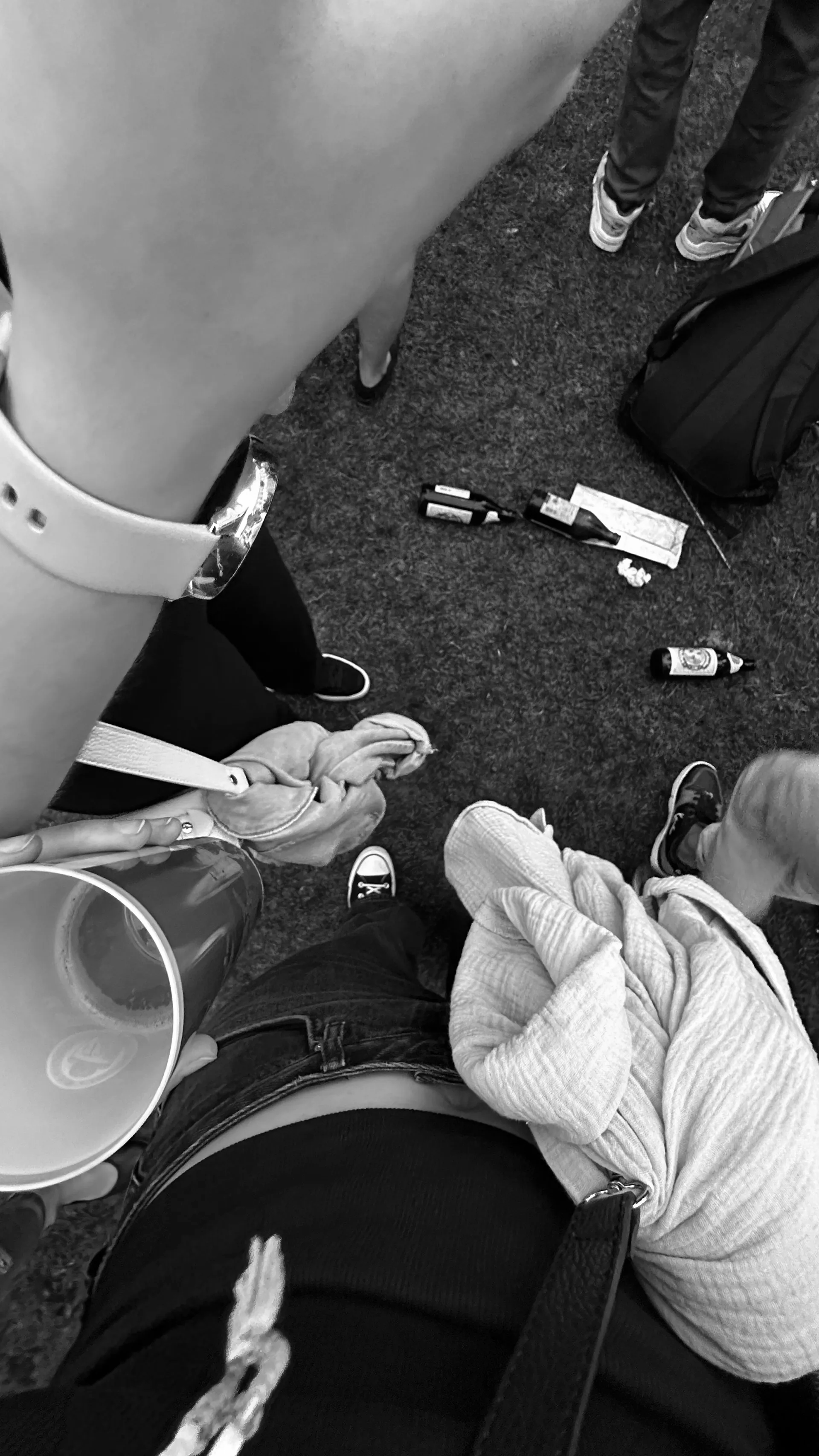 Luftaufnahme von Menschen auf einer Rasenfläche. Einige halten Getränke und Flaschen, bei anderen sind die Füße zu sehen.