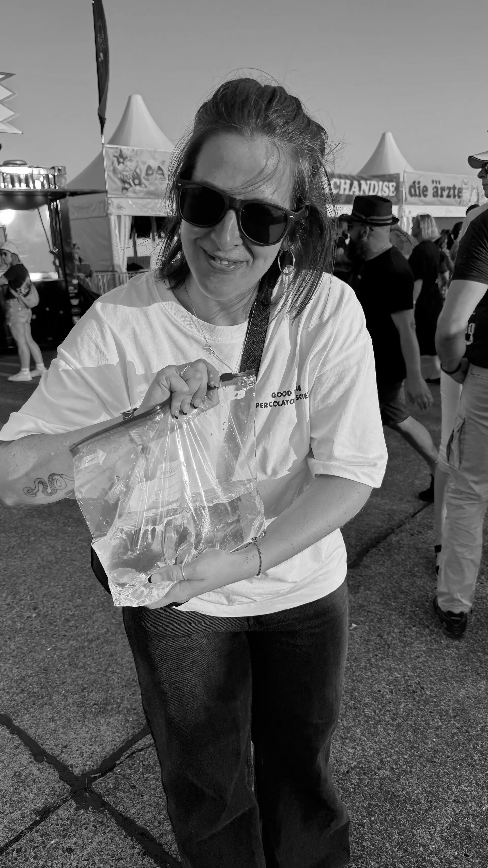 Sabrina mit einem verschlossenen Zipper-Beutel in der Hand (gefüllt mit Wasser), lächelnd bei einer Veranstaltung im Freien.