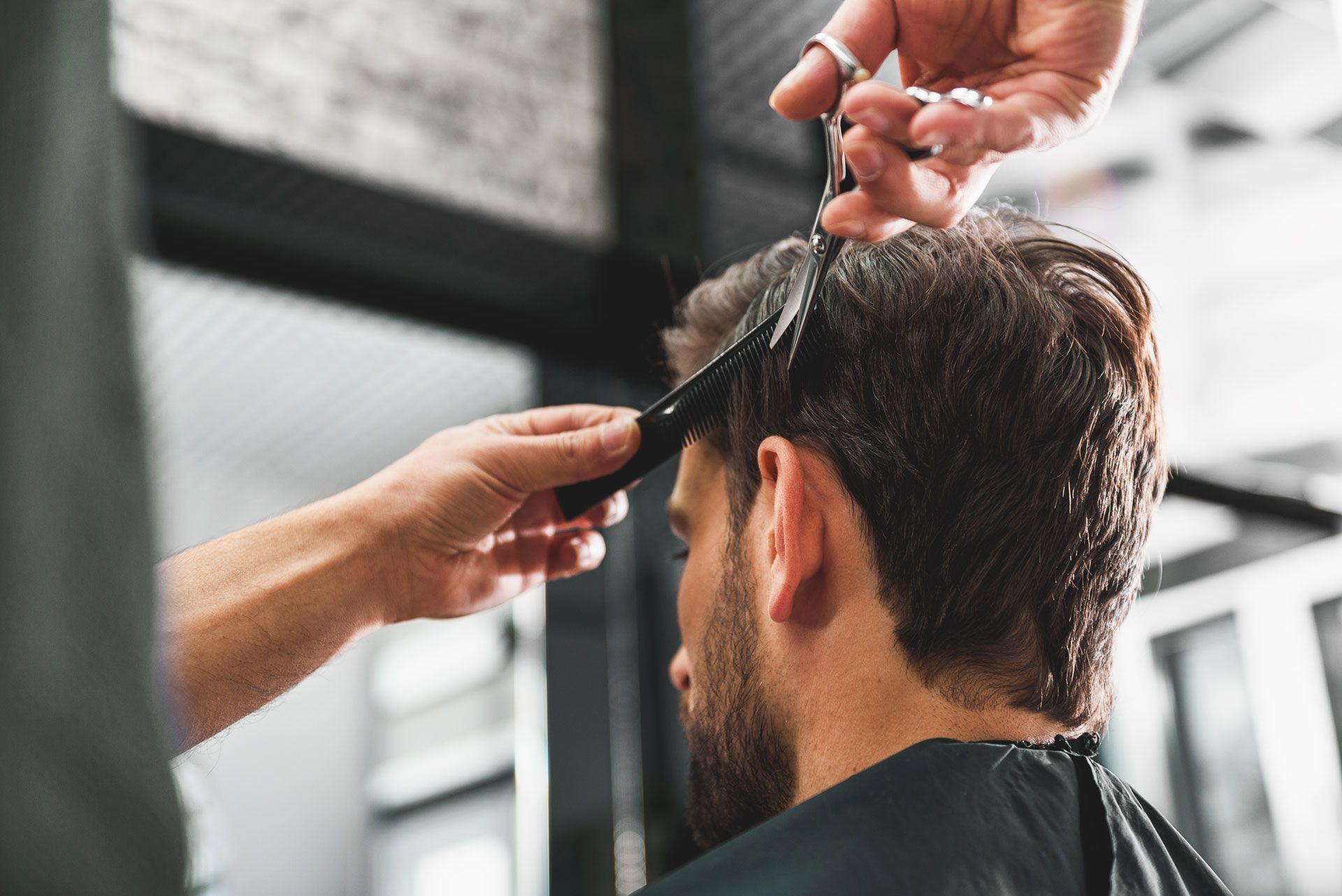A barber uses scissors to trim the hair of a client in a well-lit salon.