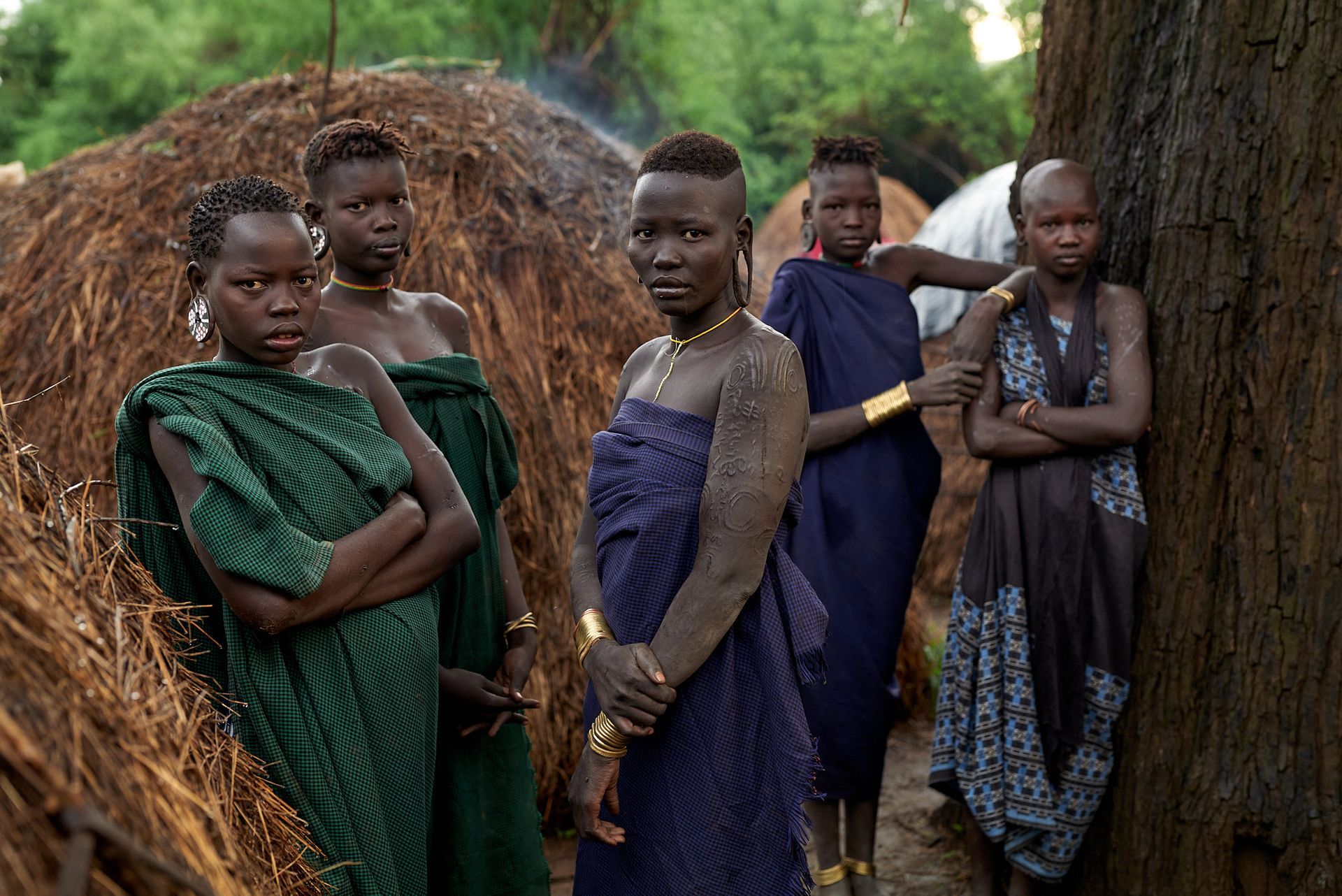 A group of Mursi women in traditional attire standing by a haystack in Ethiopia's Omo Valley.