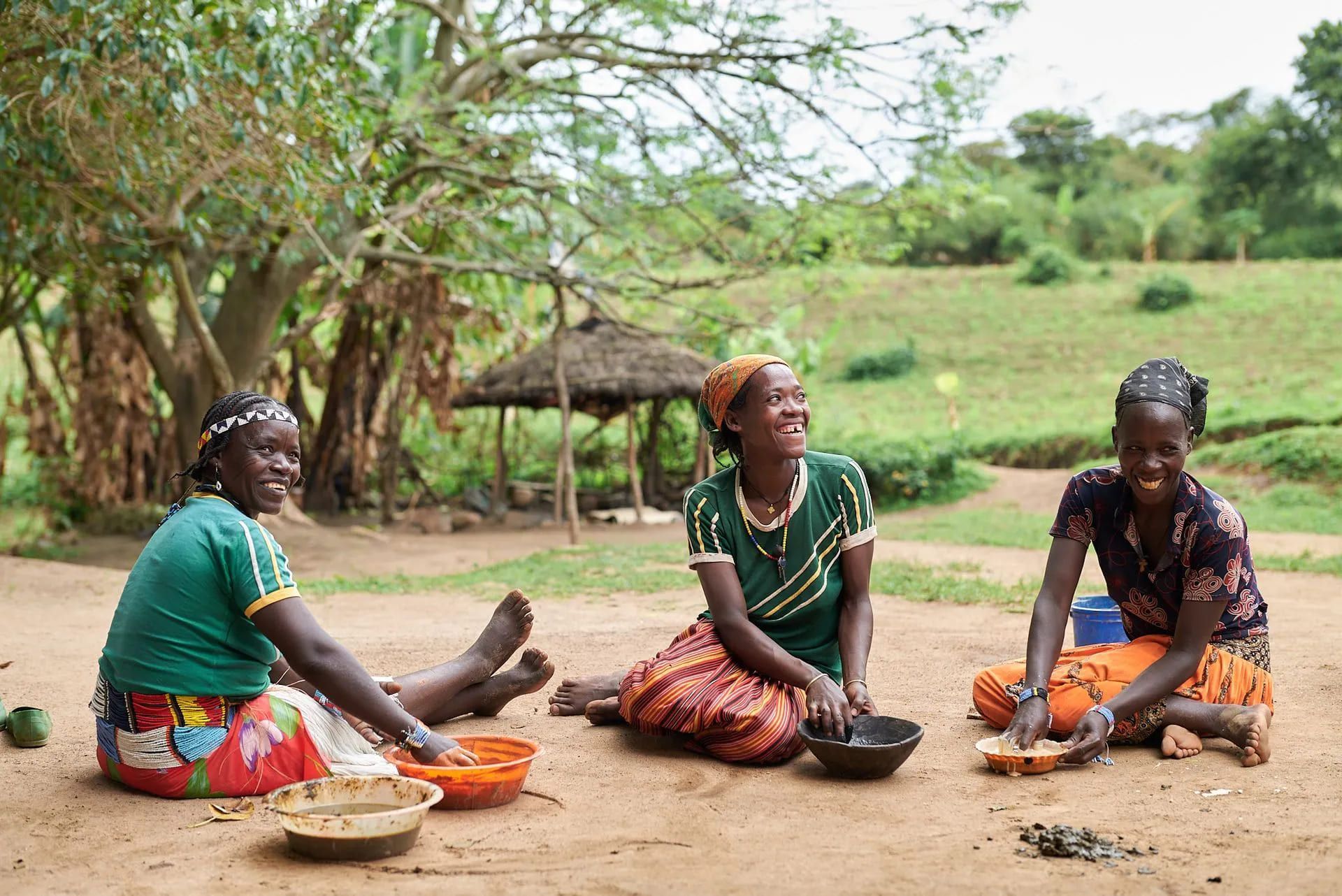 Three women are sitting on the ground with bowls of food.