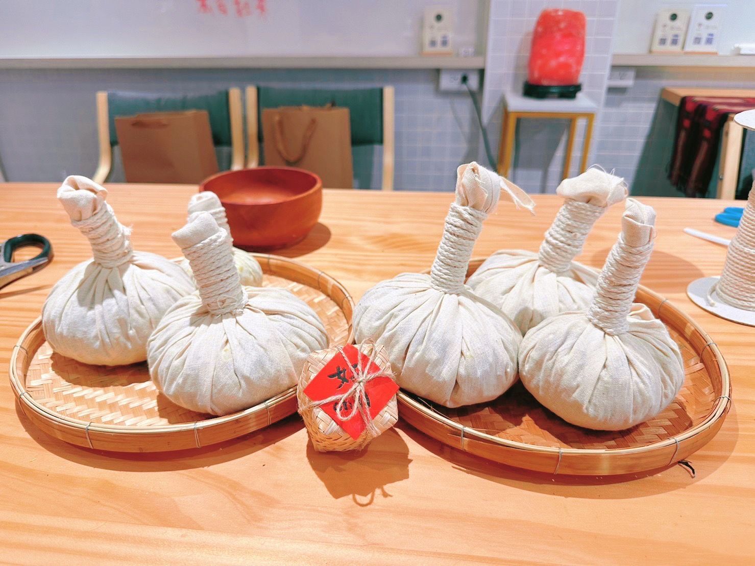 桌上放著六個草本熱敷球，放在木托盤上，旁邊還有剪刀和木碗。