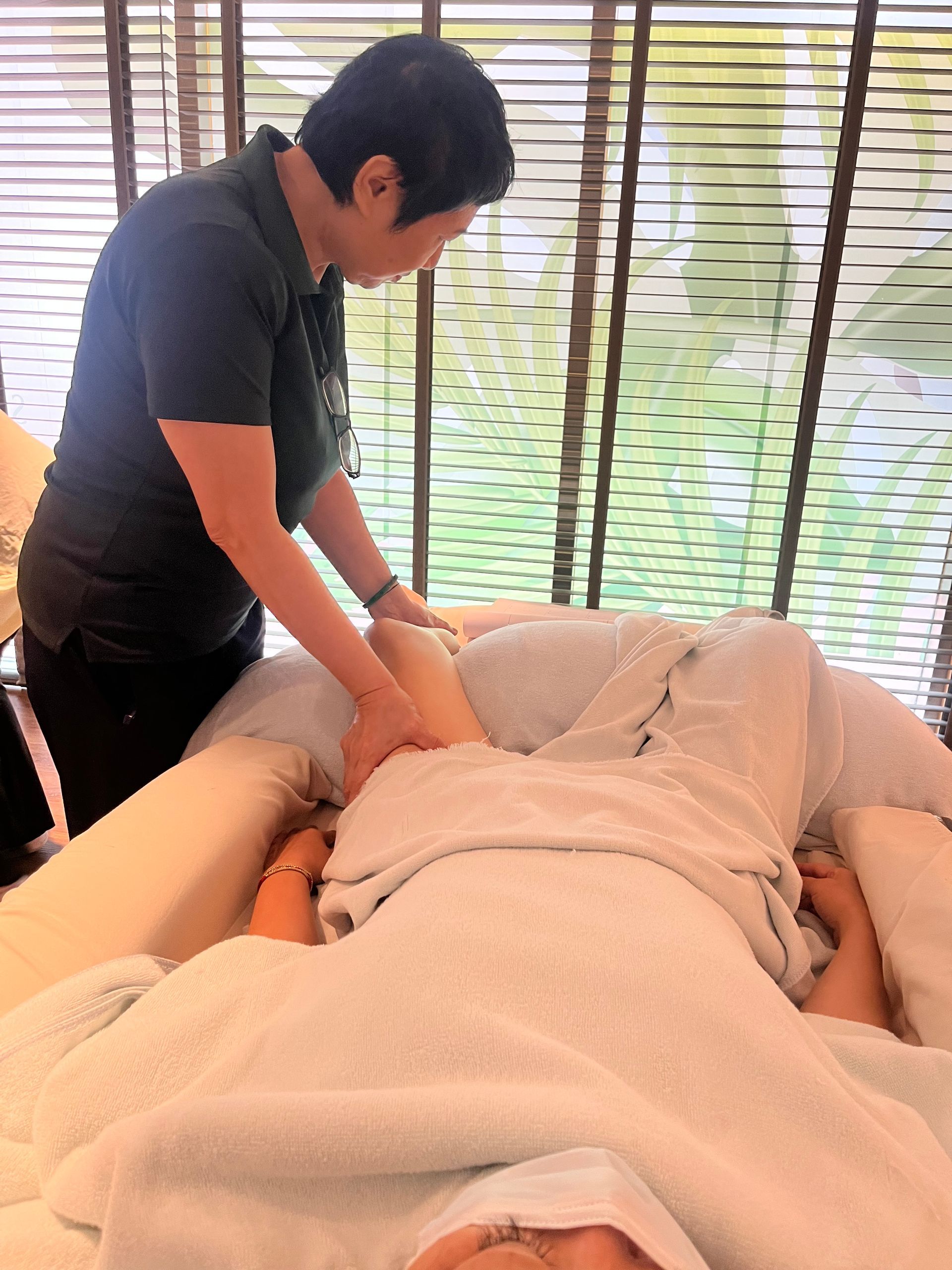 一名男子正在為躺在按摩床上的人做腿部按摩。場景似乎是在水療中心。