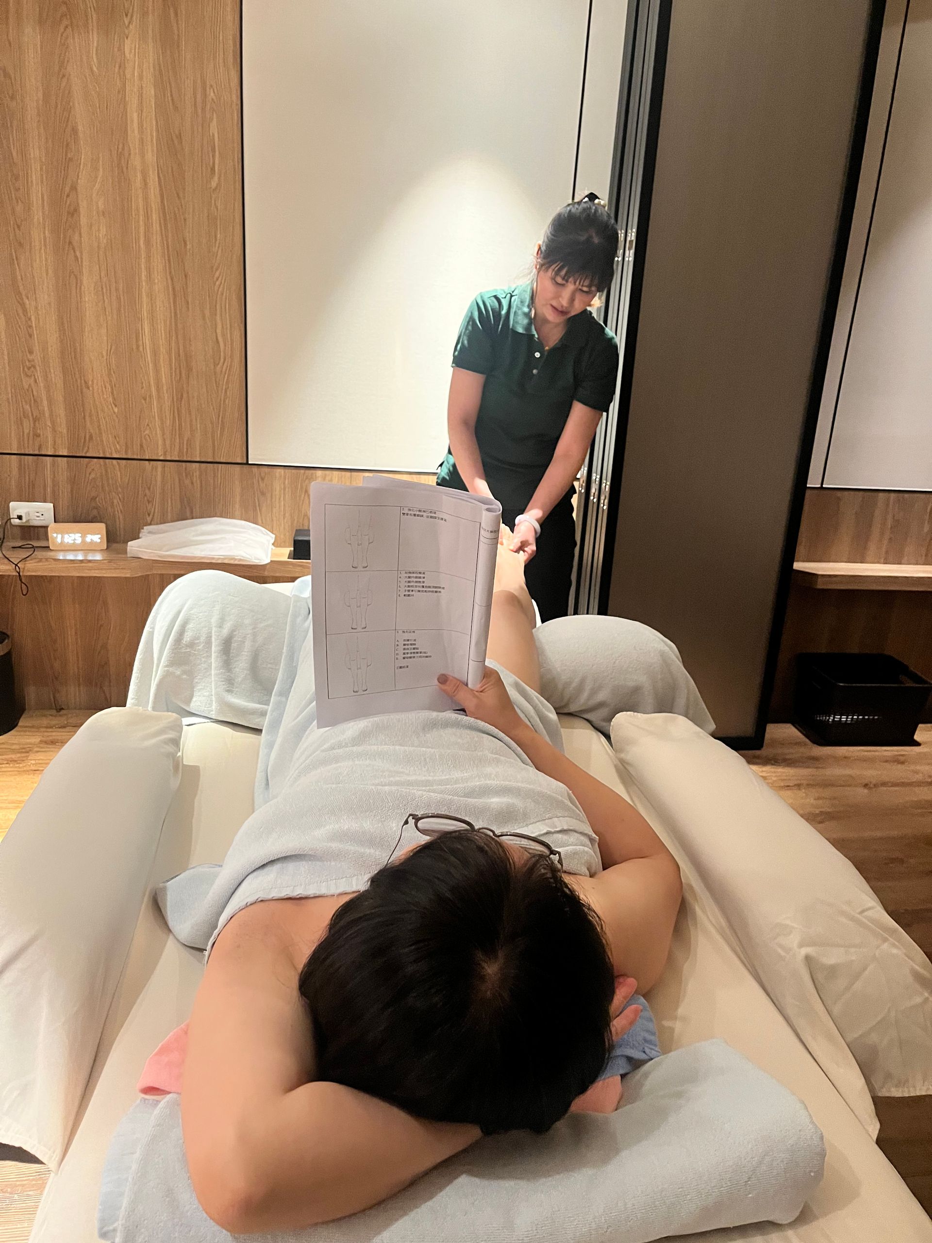 一位顧客躺在按摩床上接受足部按摩。按摩師站在他/她上方。