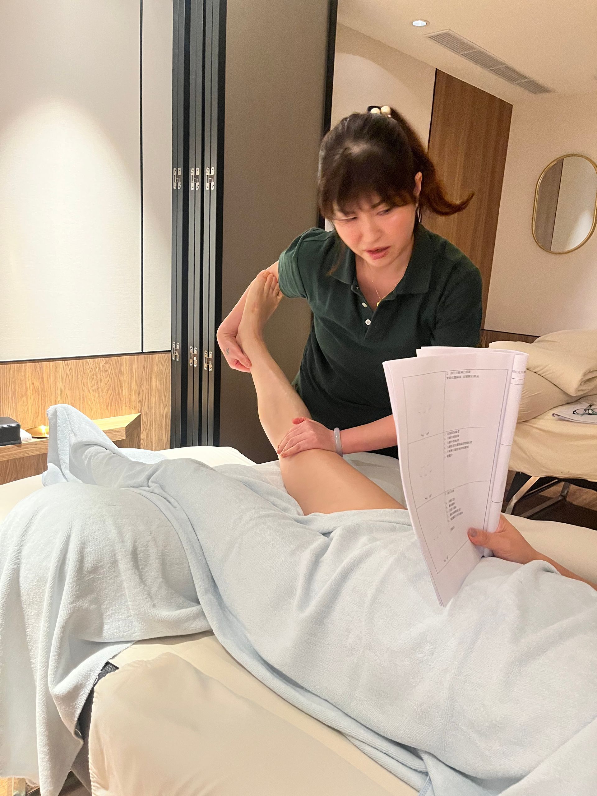 在光線充足的房間裡,有人一邊拿著文件一邊給人腿部按摩。