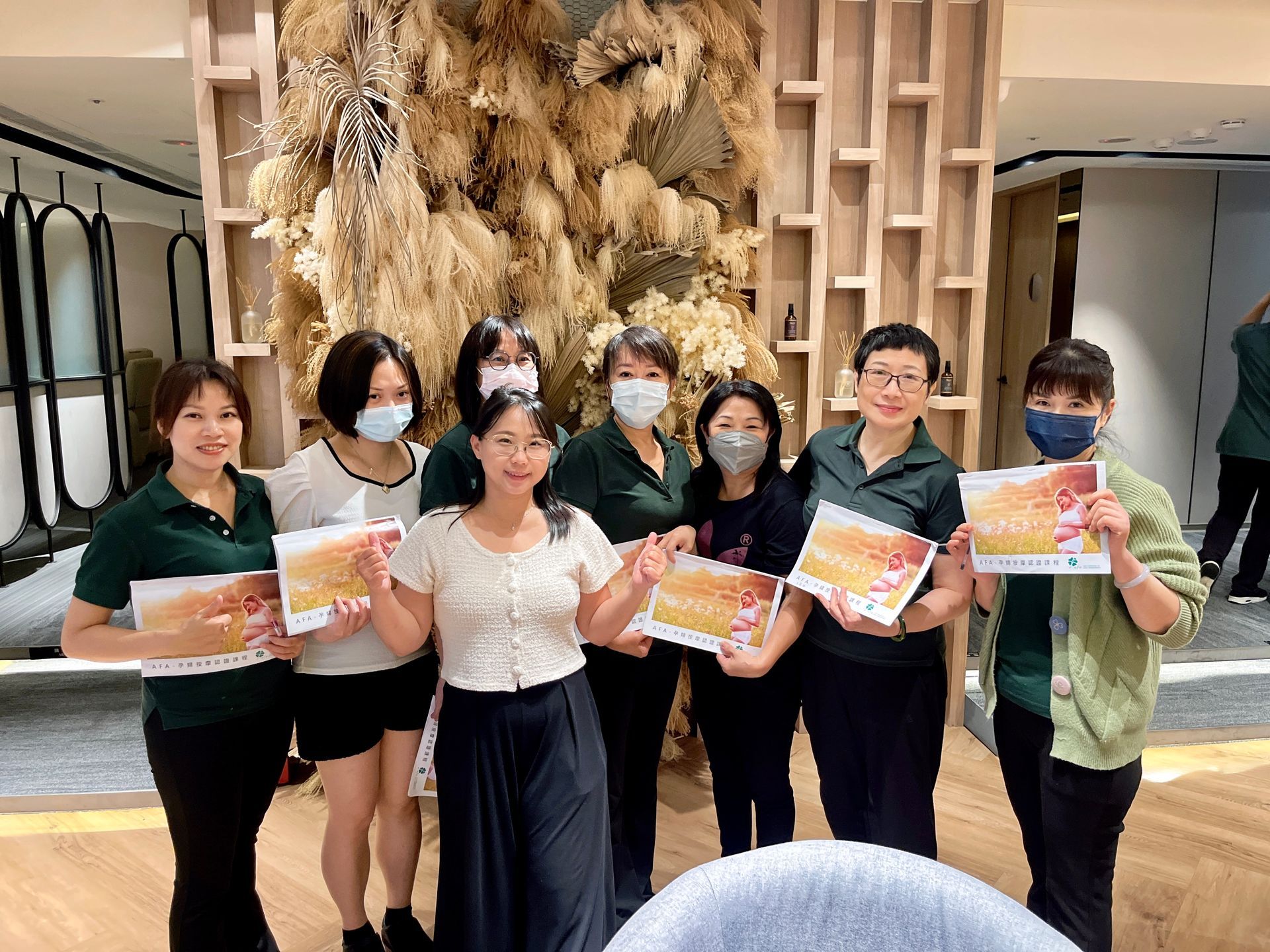 一群微笑的女性手持傳單，站在一個現代、光線充足的室內，室內裝飾著木板和乾燥花。