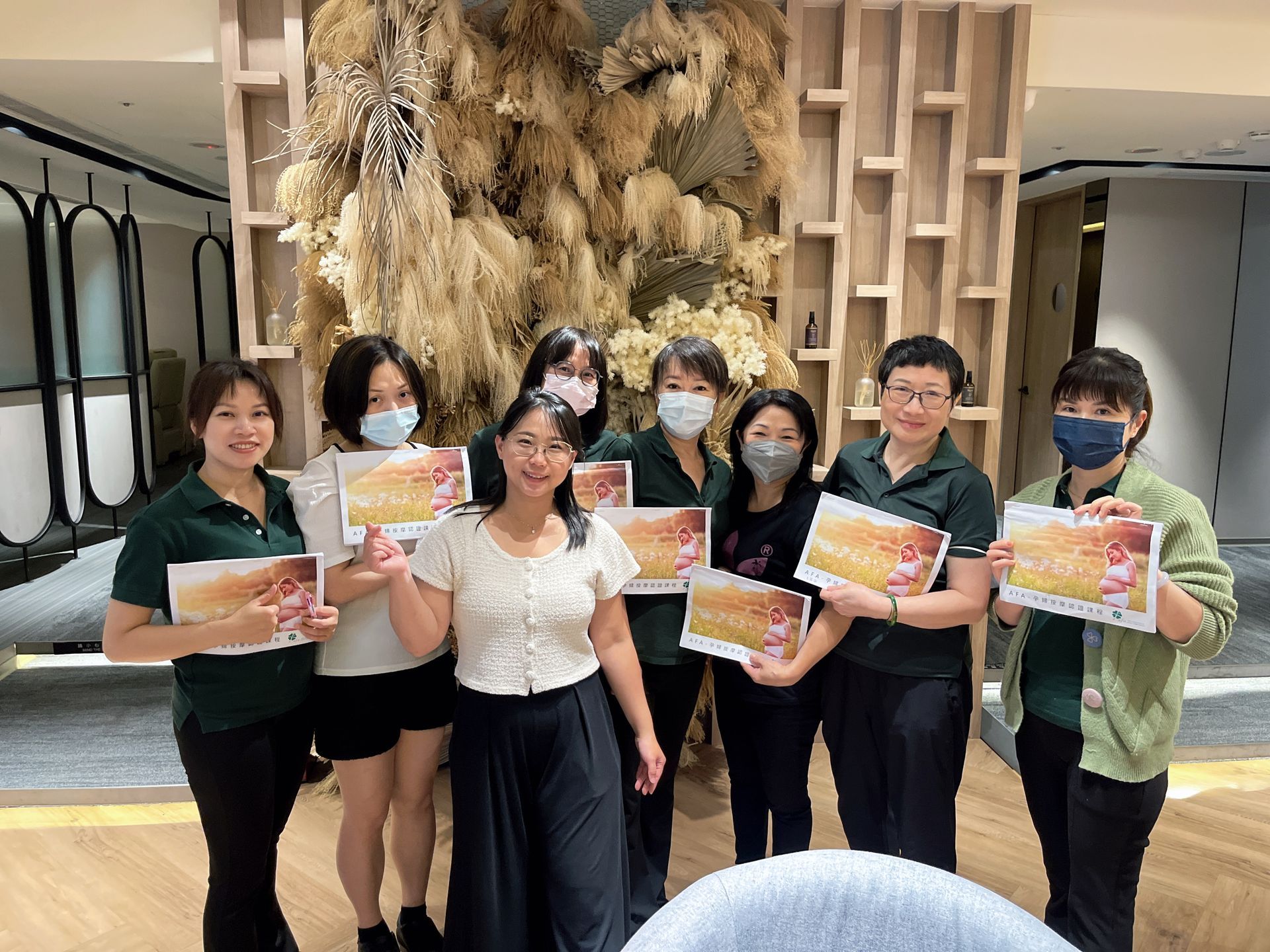 一群人手持證書，面帶微笑，置身於擺放著裝飾植物的現代室內空間。