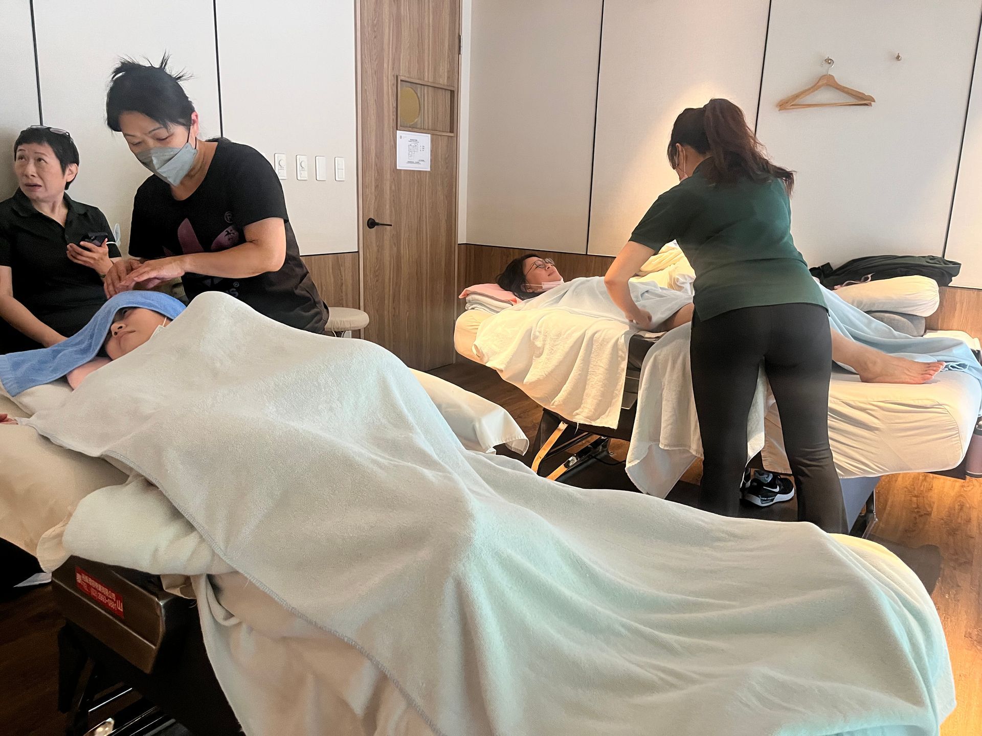 人們躺在按摩床上接受按摩,按摩師正在工作。明亮的室內環境。