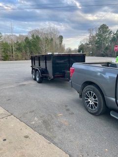 Black trailer hitched to a gray pickup on a roadside beside a stop sign and trees