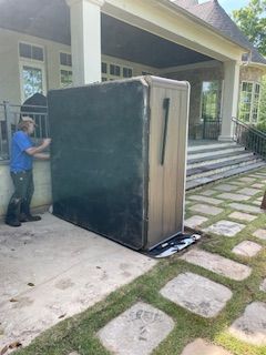 Man moving a large black and beige appliance through a driveway beside a house
