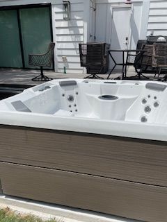 White outdoor hot tub on a patio with chairs and a sliding glass door in the background