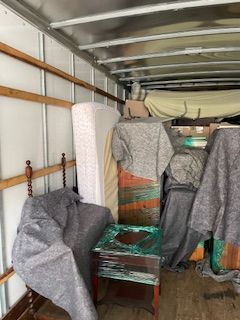 Covered furniture and packed items inside a moving truck with white walls and metal ceiling.