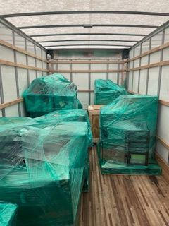 Green-wrapped furniture inside a moving truck with wood flooring and metal walls
