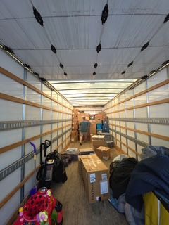 Inside an empty moving truck, boxes and bags are stacked along the walls.