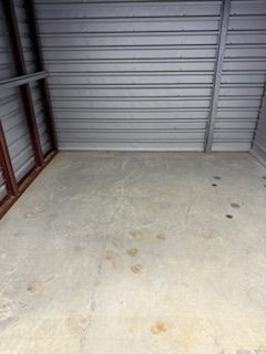 Empty concrete-floored storage unit with gray metal walls and a brown frame on the left