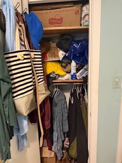 Packed closet with hanging clothes, boxes, and bags on crowded shelves