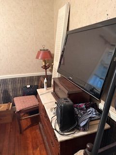 Living room corner with large TV on a white console, red lamp, bench, and hardwood floor
