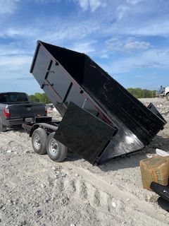 Black dump trailer tipped steeply on a gravel lot under a blue sky