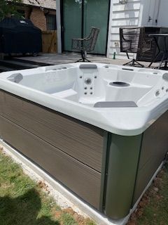 Outdoor hot tub with gray siding and white interior on a patio beside a house
