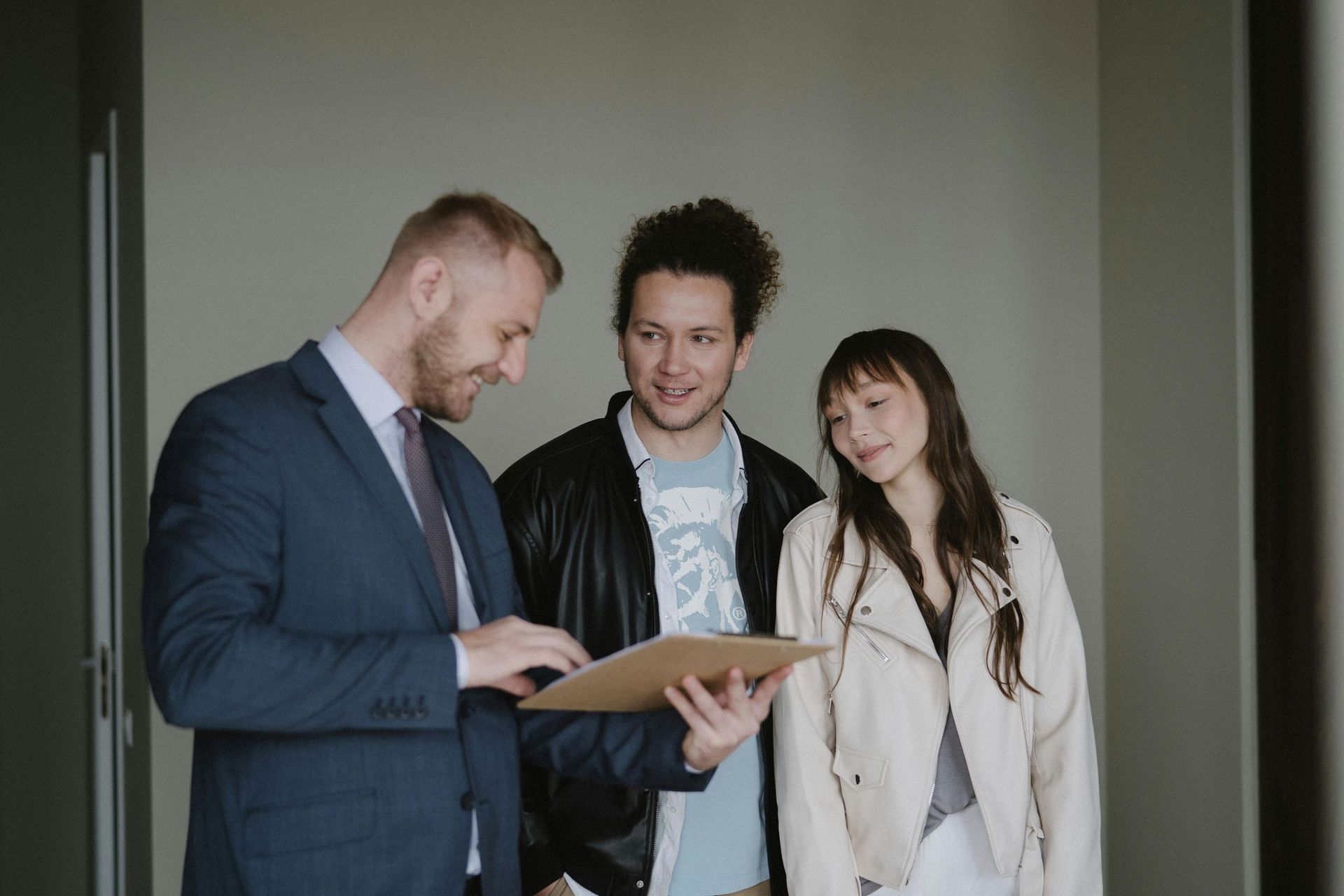 A man in a suit shows a document to a couple in an indoor setting, with all three looking at the paper.
