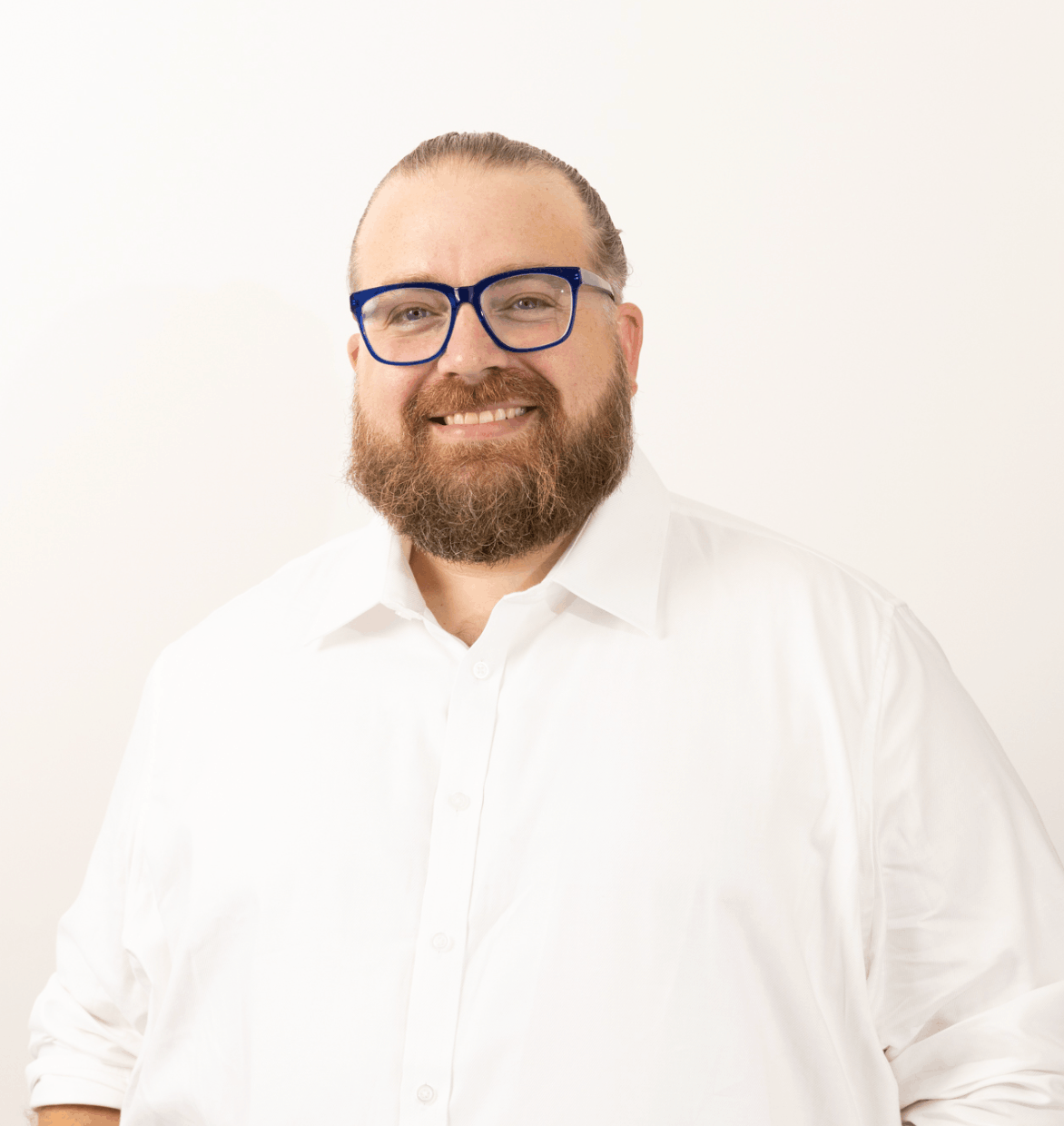 Smiling man with glasses and beard, wearing a white shirt, against a white background.