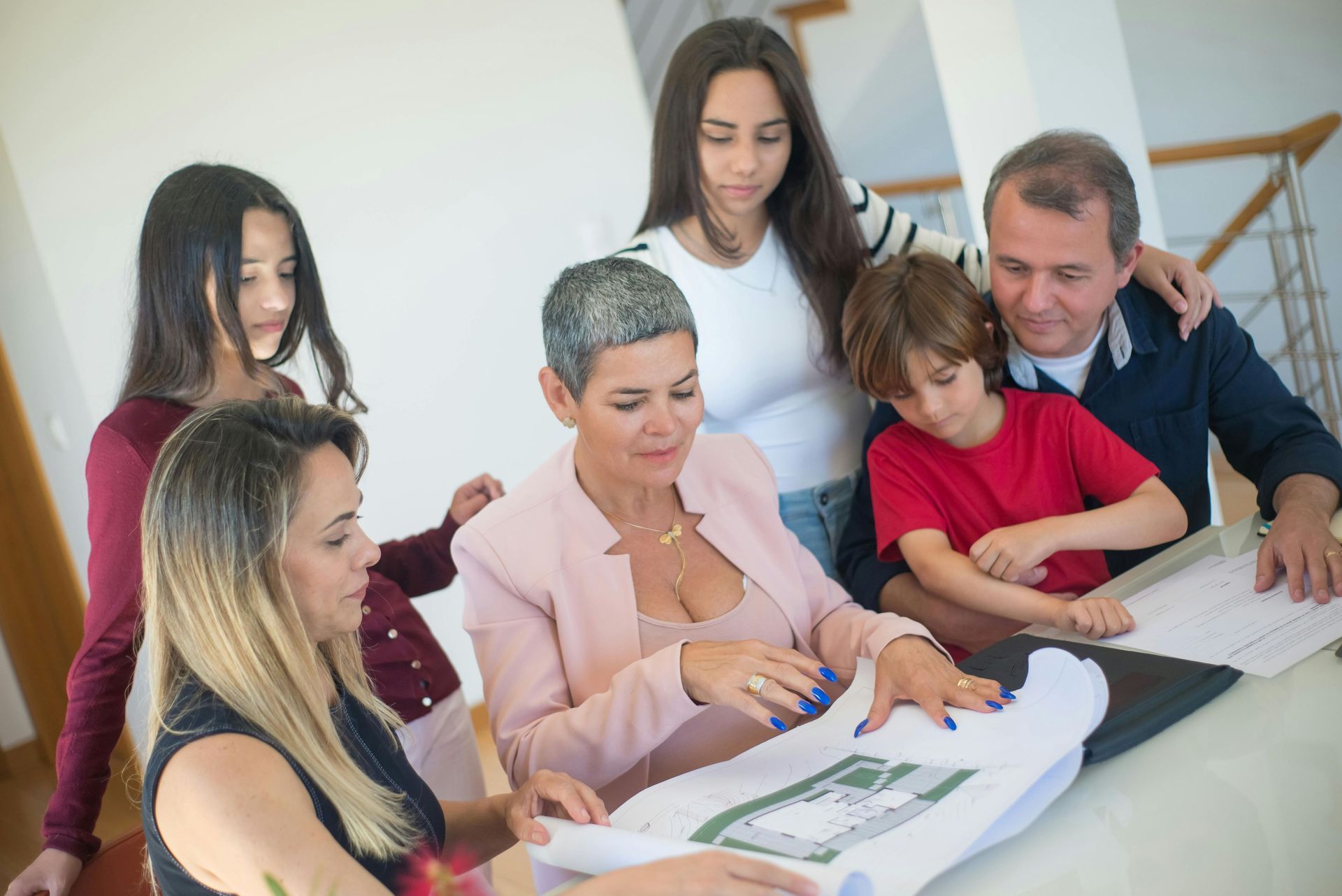 A group of people standing around a table, reviewing house blueprints together in a bright, modern interior.