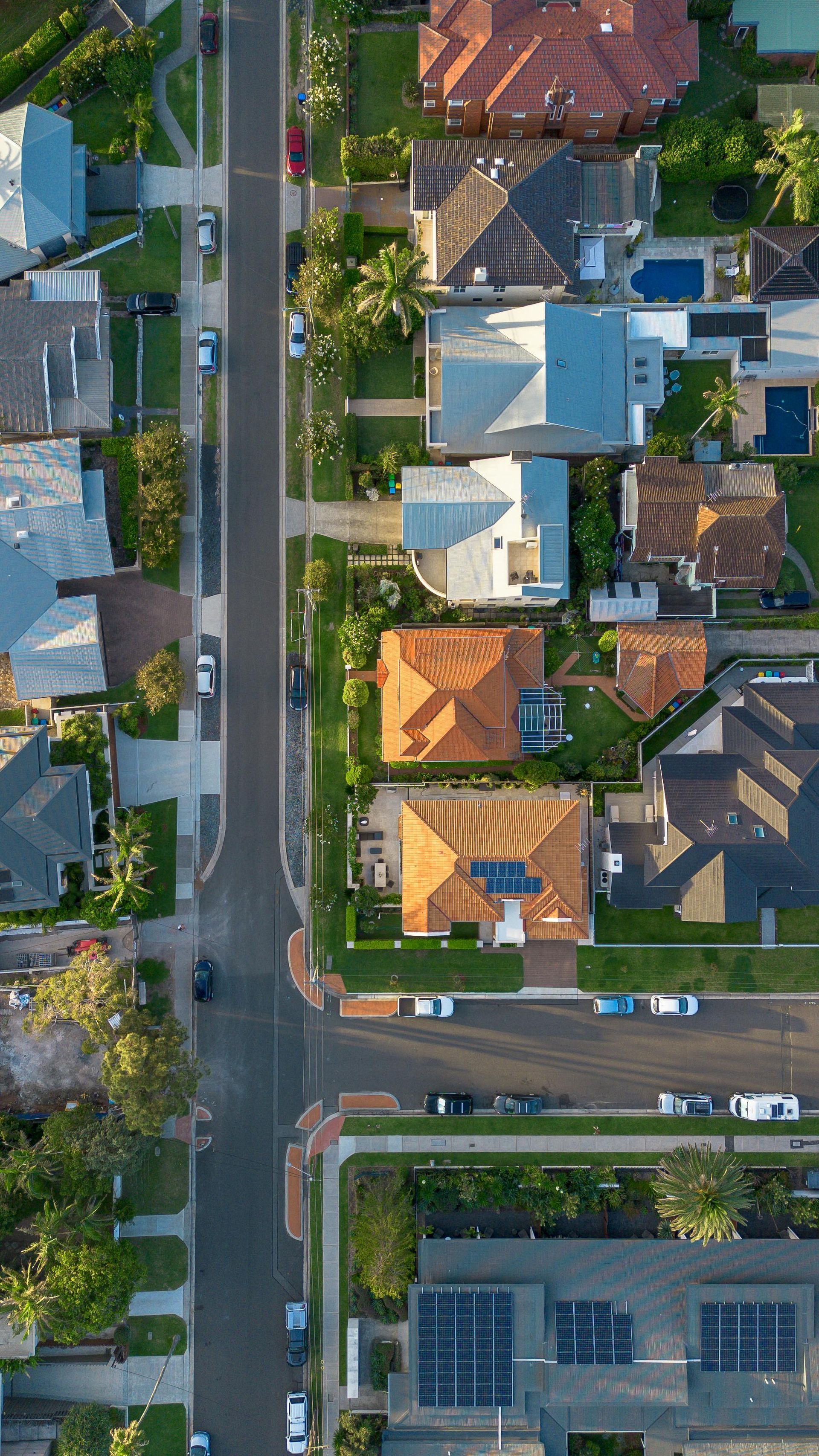 An aerial view of a suburban street intersection with houses, driveways, and trees lining the roads.