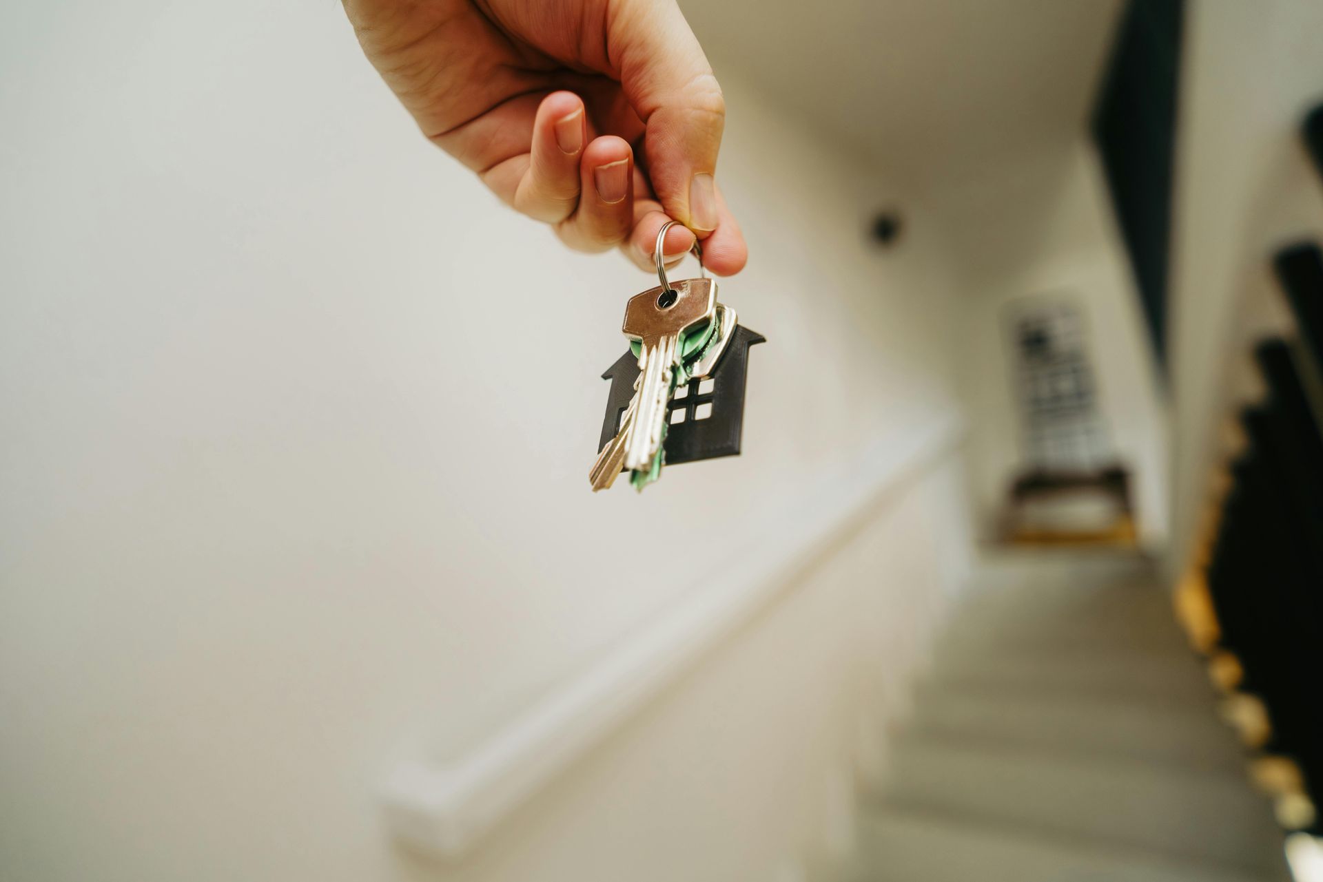a hand holding out a house key towards a staircase.