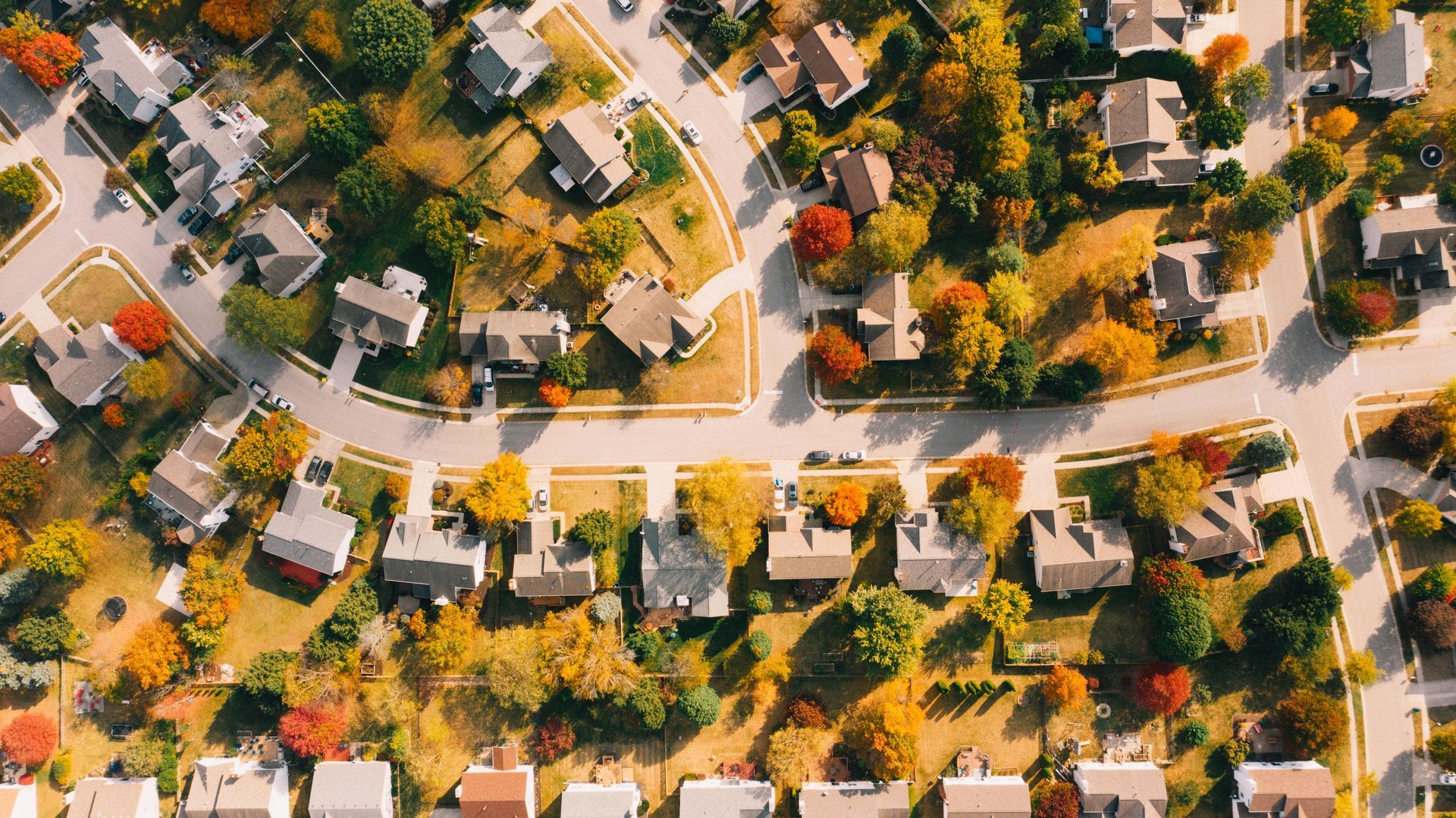 Aerial view of a residential neighborhood during autumn, with houses surrounded by trees with yellow and orange foliage.
