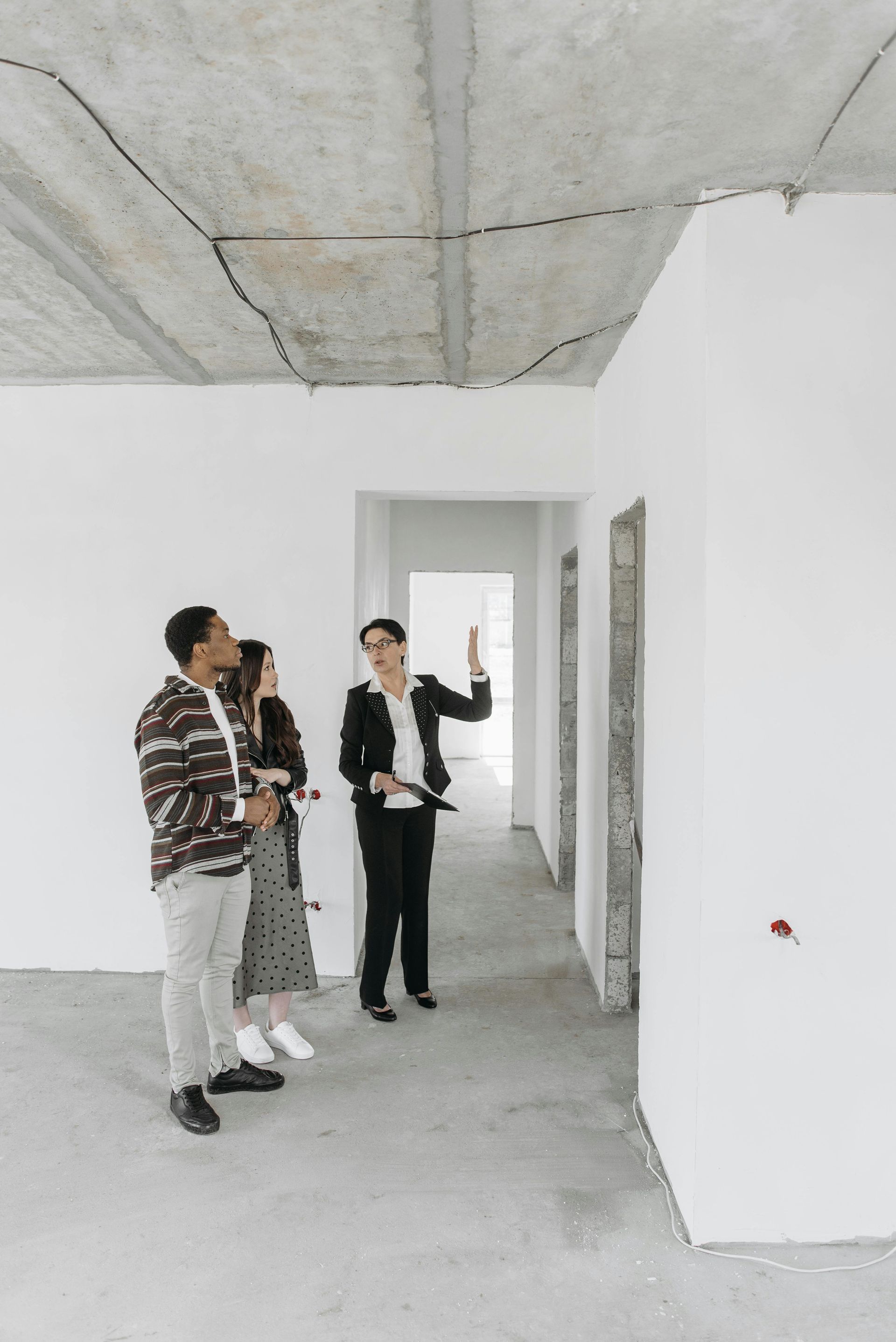 A female agent wearing a hard hat inspecting an empty house along with a couple.