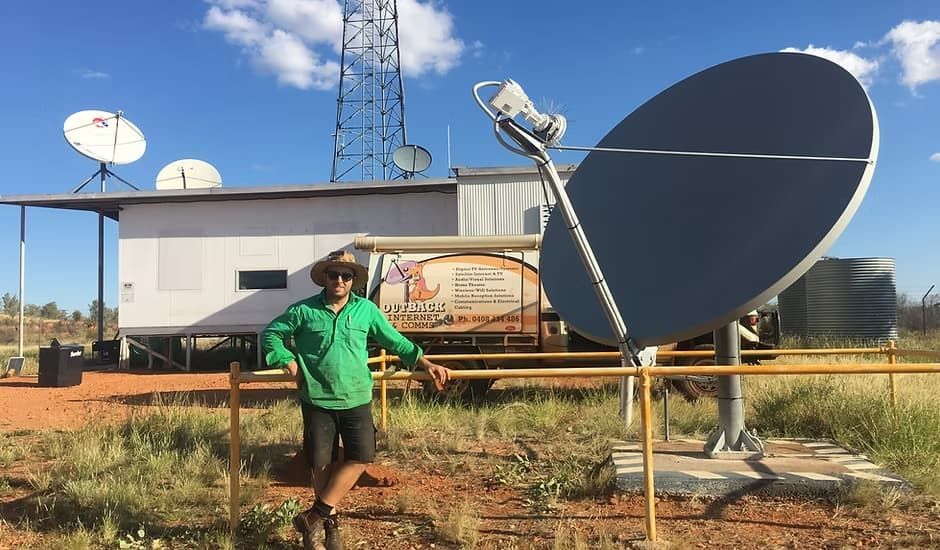 A Man In A Green Shirt Is Standing In Front Of A Large Satellite Dish — Outback Internet & Comms In Ciccone, NT