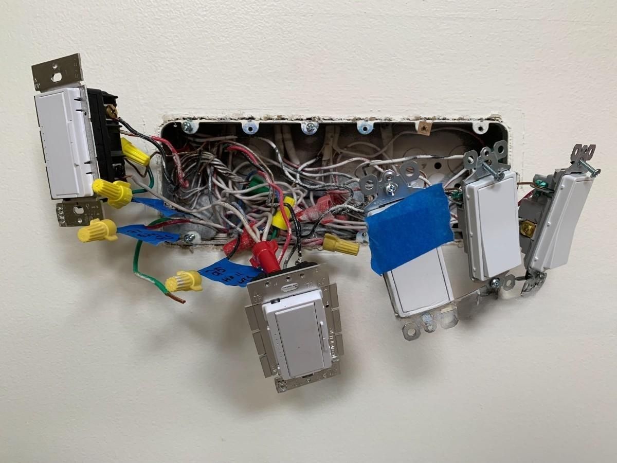 Electrical box with exposed wires and multiple light switches in a wall.