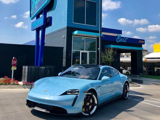Light blue Porsche in front of a blue car wash building with signage.