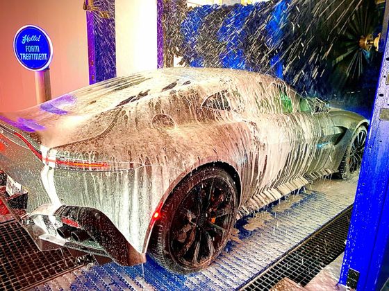 Silver sports car covered in foamy soap at a car wash.