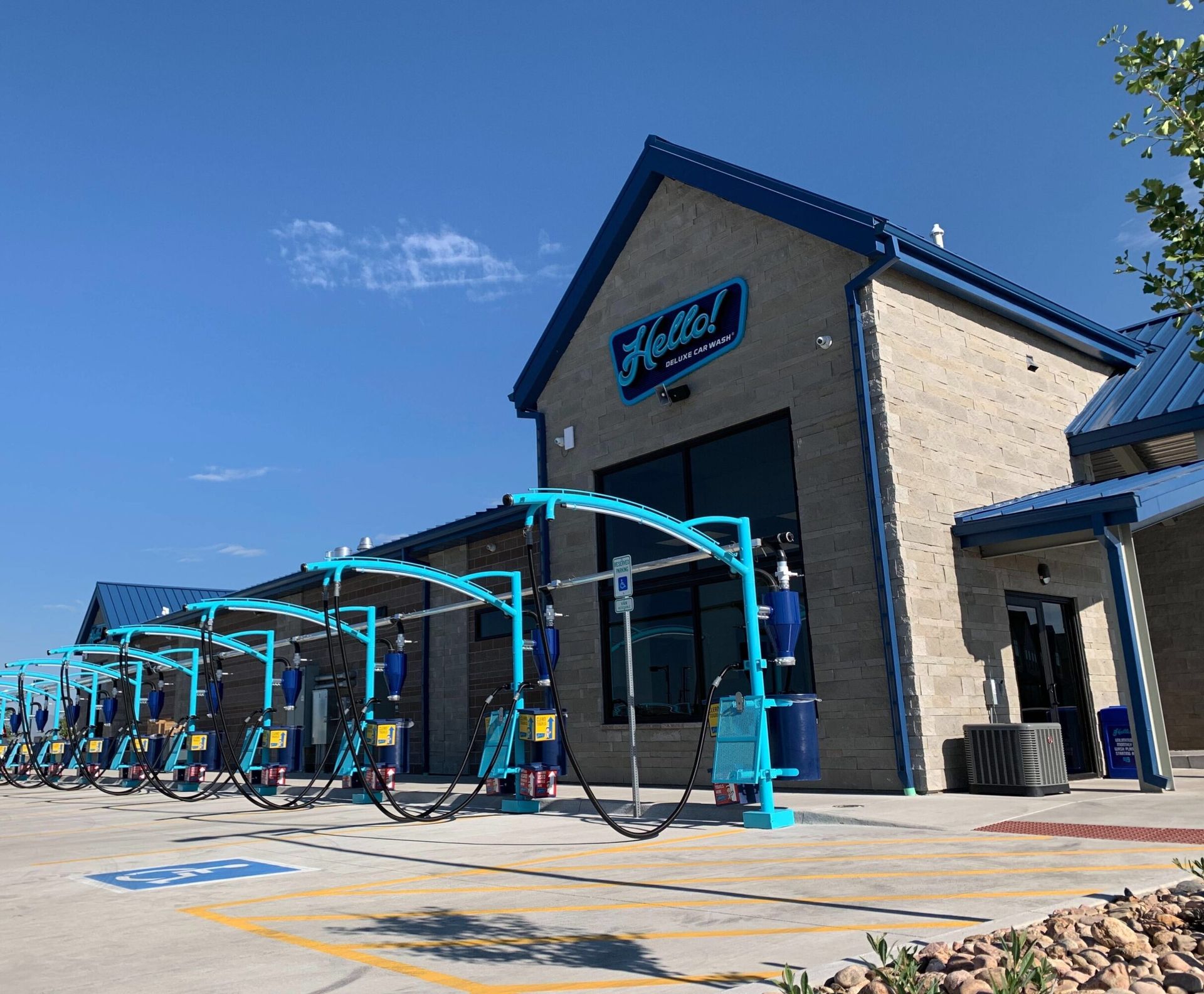Exterior of a car wash facility with multiple bays and blue and teal accents. Clear blue sky.