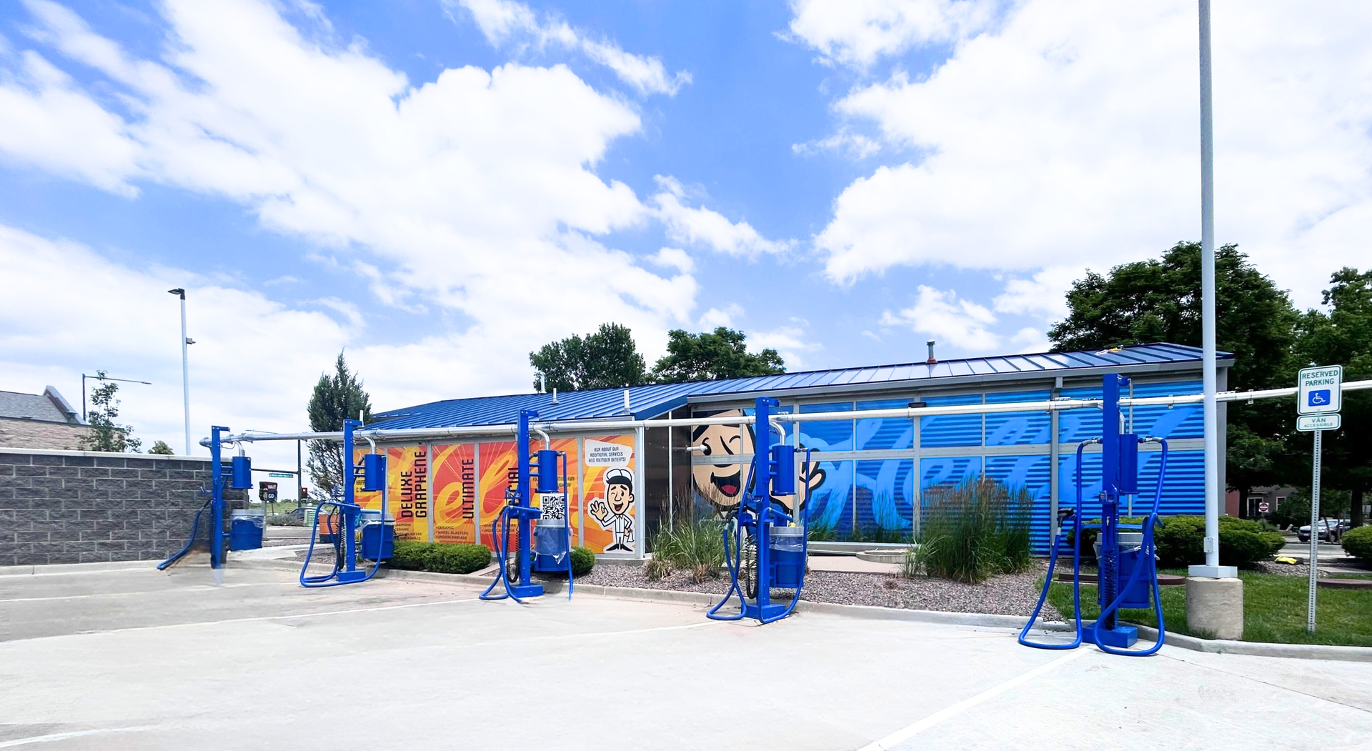 Exterior view of a bright blue car wash with colorful art under a partly cloudy sky.