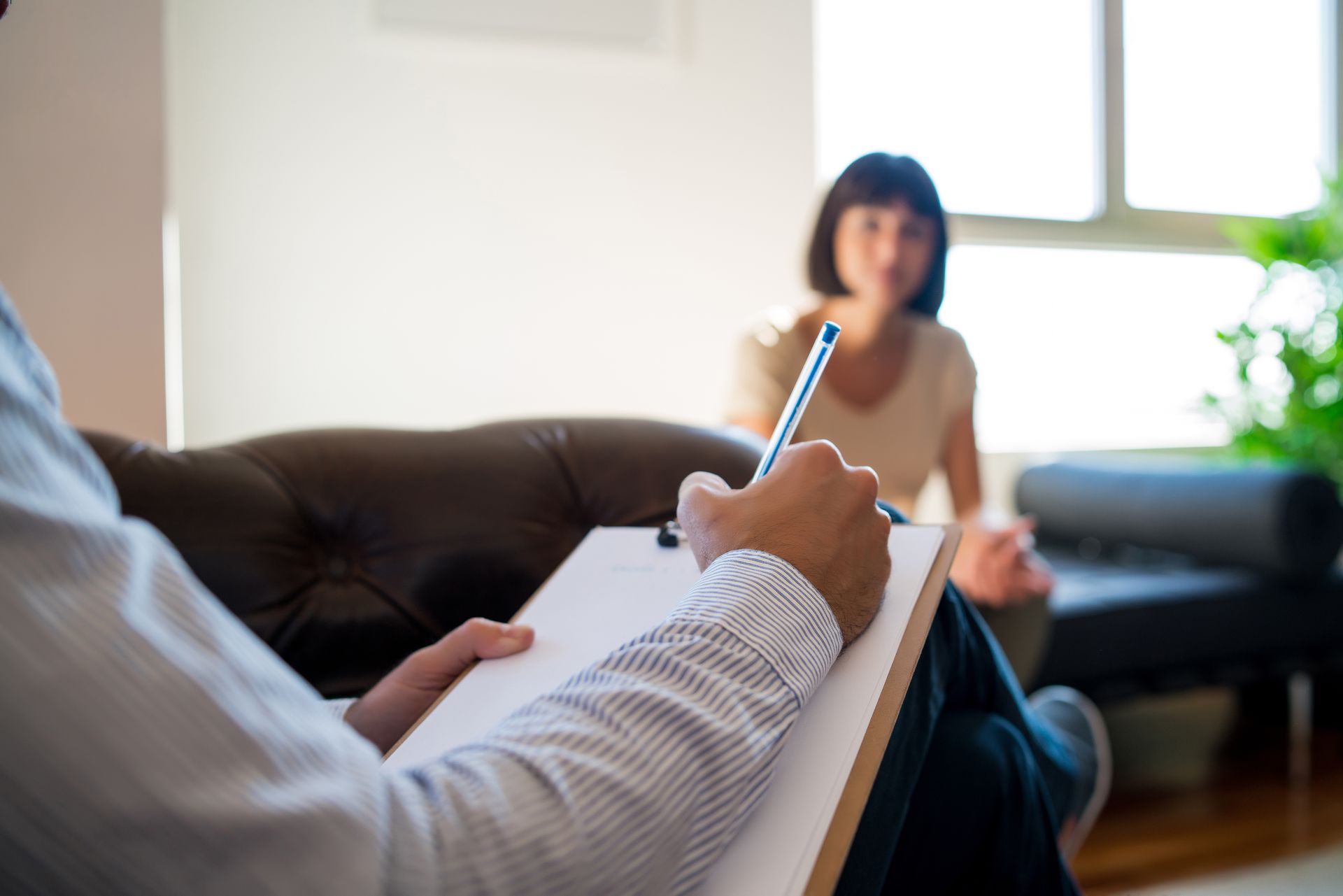 A man is writing on a clipboard while a woman sits on a couch.