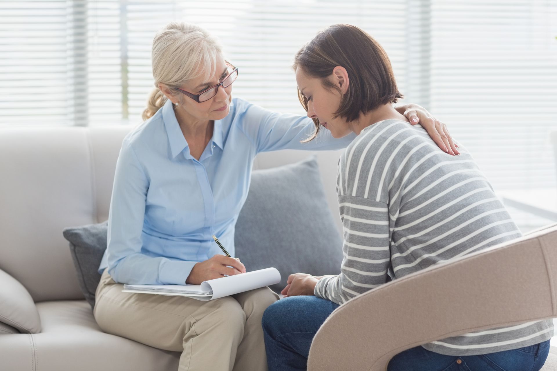 A woman is sitting on a couch talking to another woman.