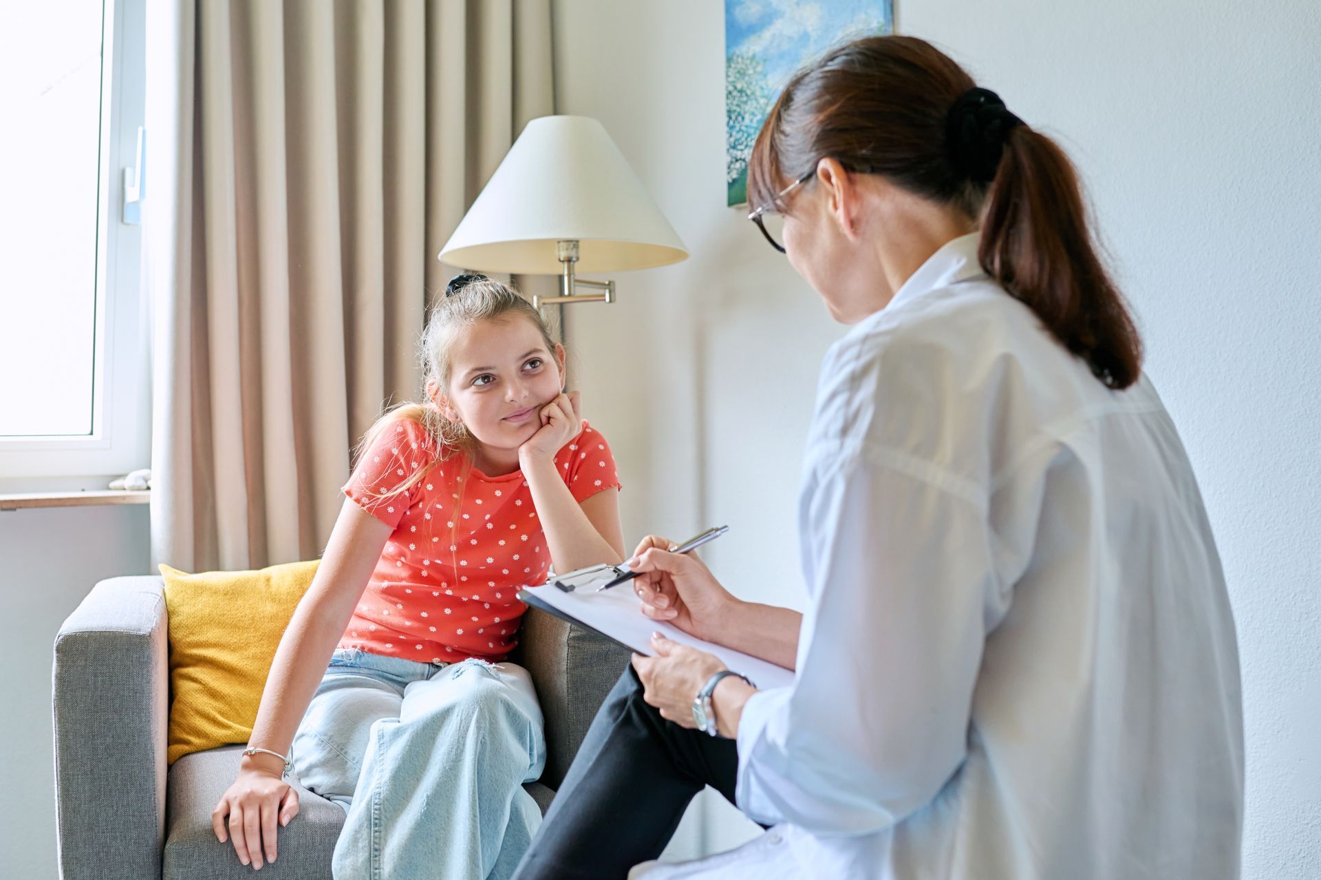 A woman is sitting on a couch talking to a young girl.