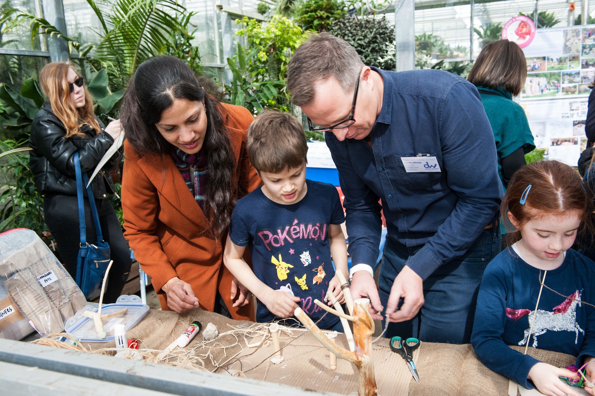 Family at an exhibit, children making a structure with an adult. Greenhouse setting.