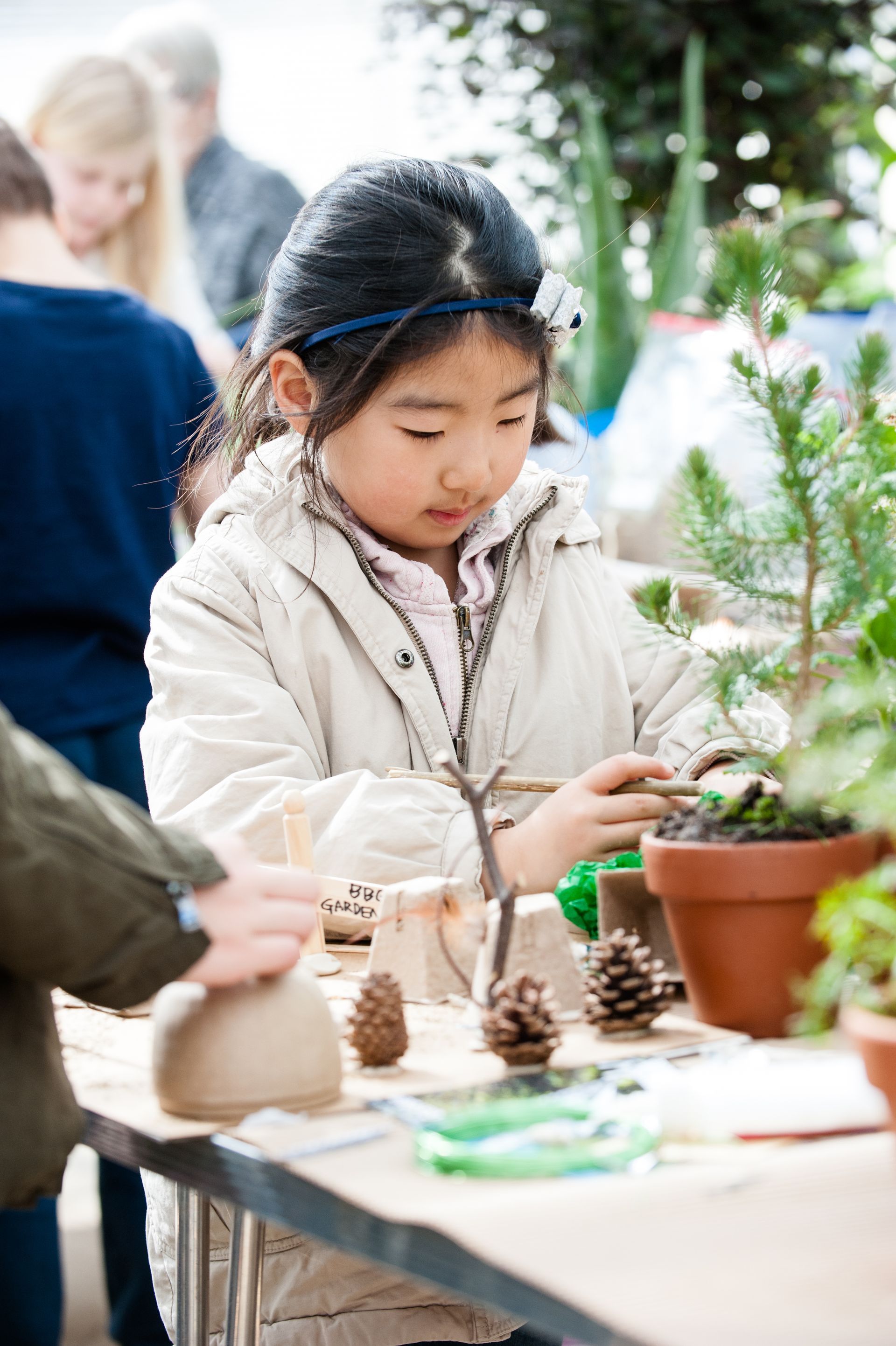 Young Asian girl crafting with natural materials on a table, focused expression.