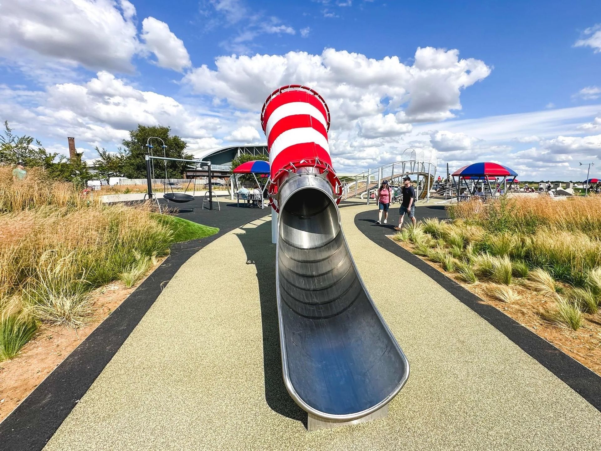 Boy in wheelchair on accessible playground bridge; smiling with caregiver nearby.