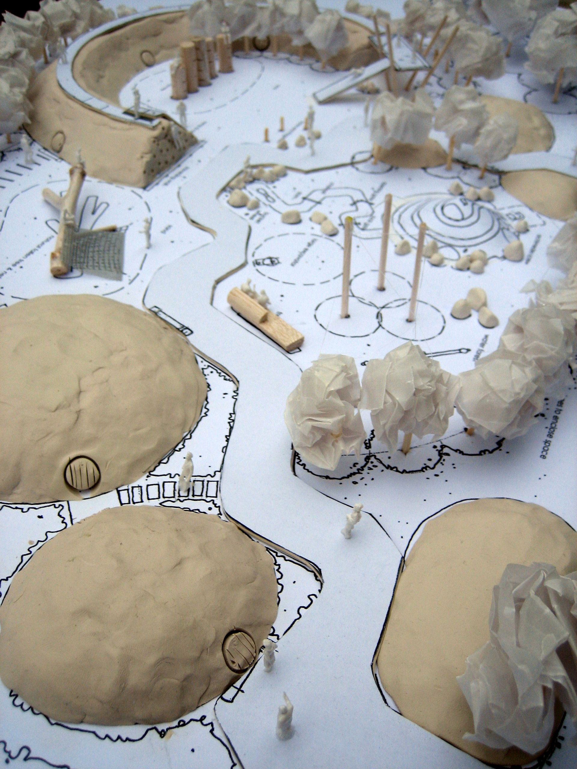 Architectural model of a park with trees, curved pathway, and small structures, on a white base.