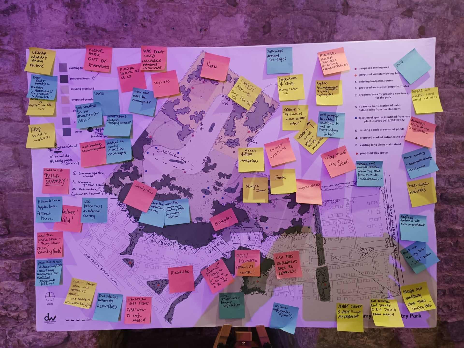 Overhead view of a park with trees, paths, a river, playground, and green open spaces.