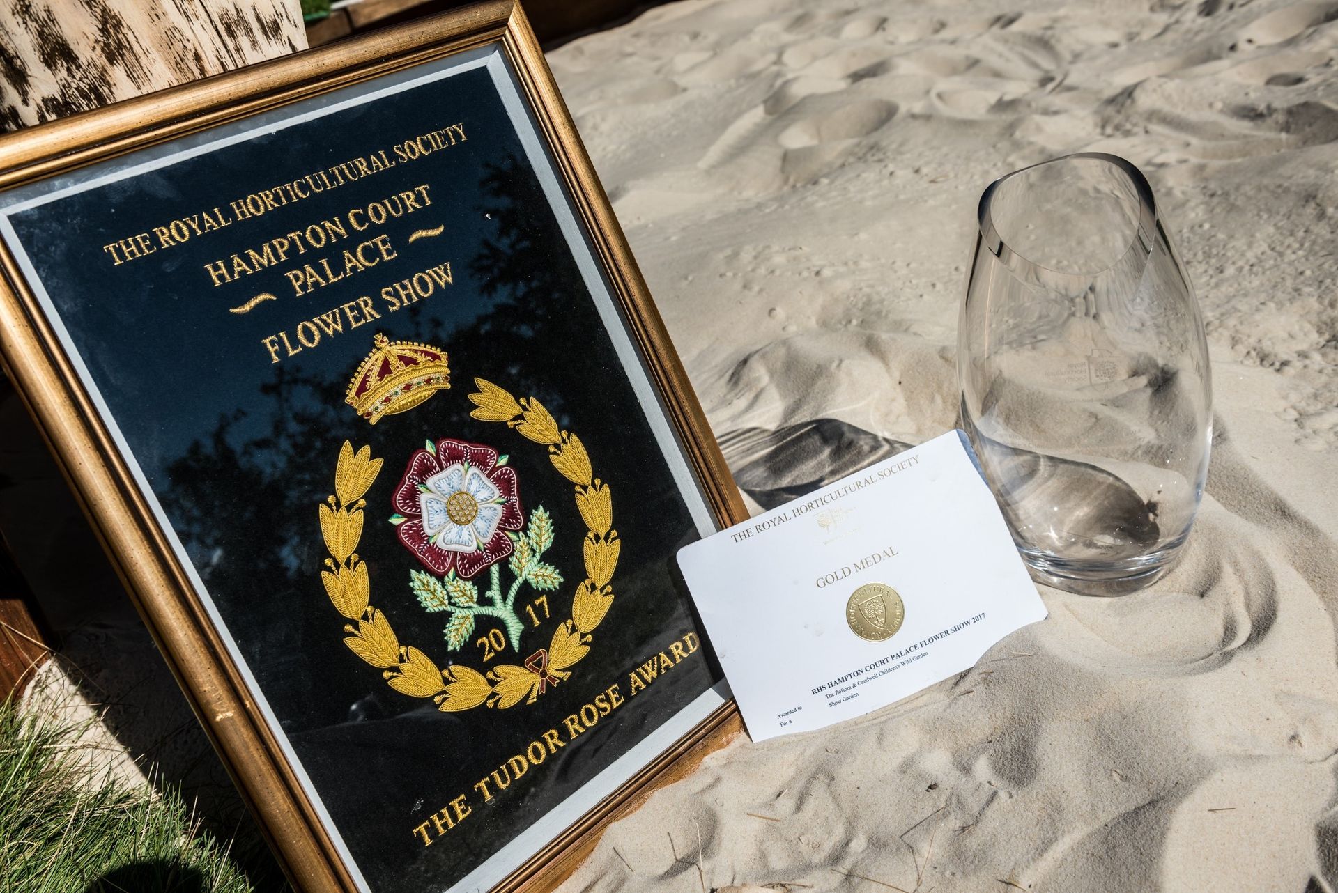 Framed sign for Hampton Court Palace, a note, and glass on sand.