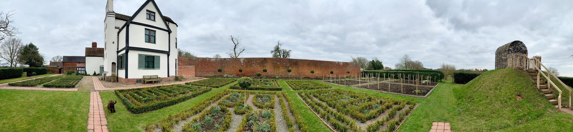 A black and white Tudor style house with a brick wall and a castle mound.