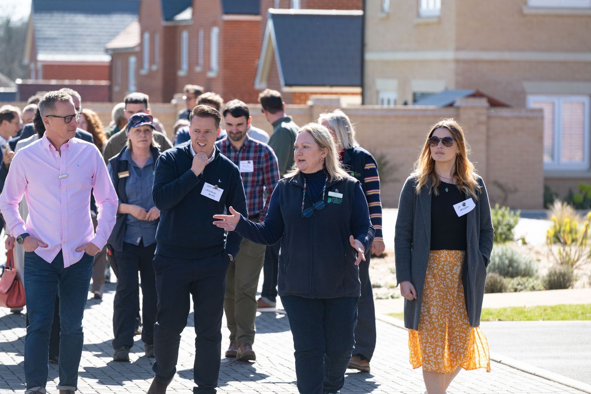 Group of people walking outside, likely on a tour. Various expressions, modern houses in the background.